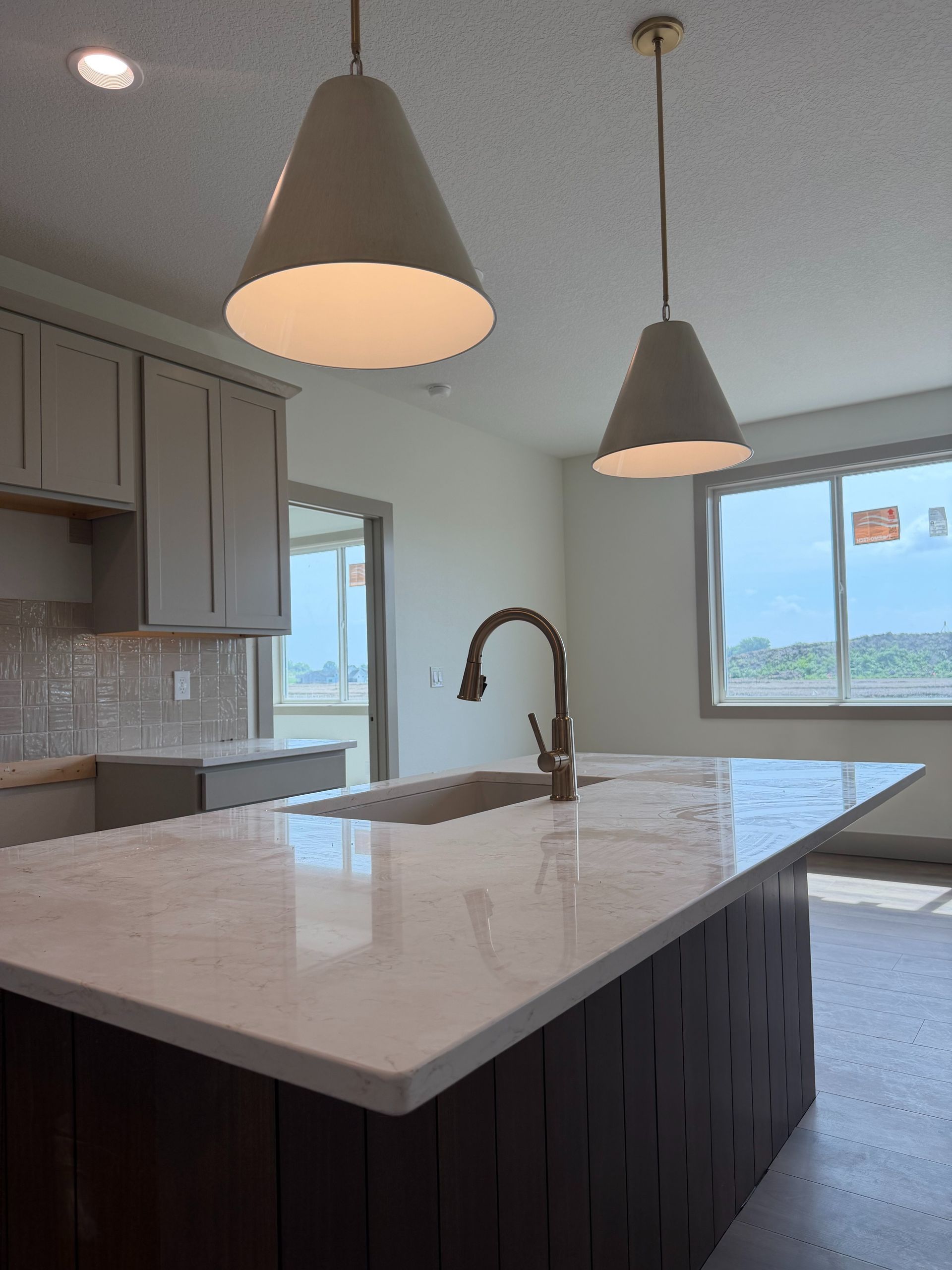 Modern kitchen with large island, pendant lights, gray cabinets, and a window view of the outdoors