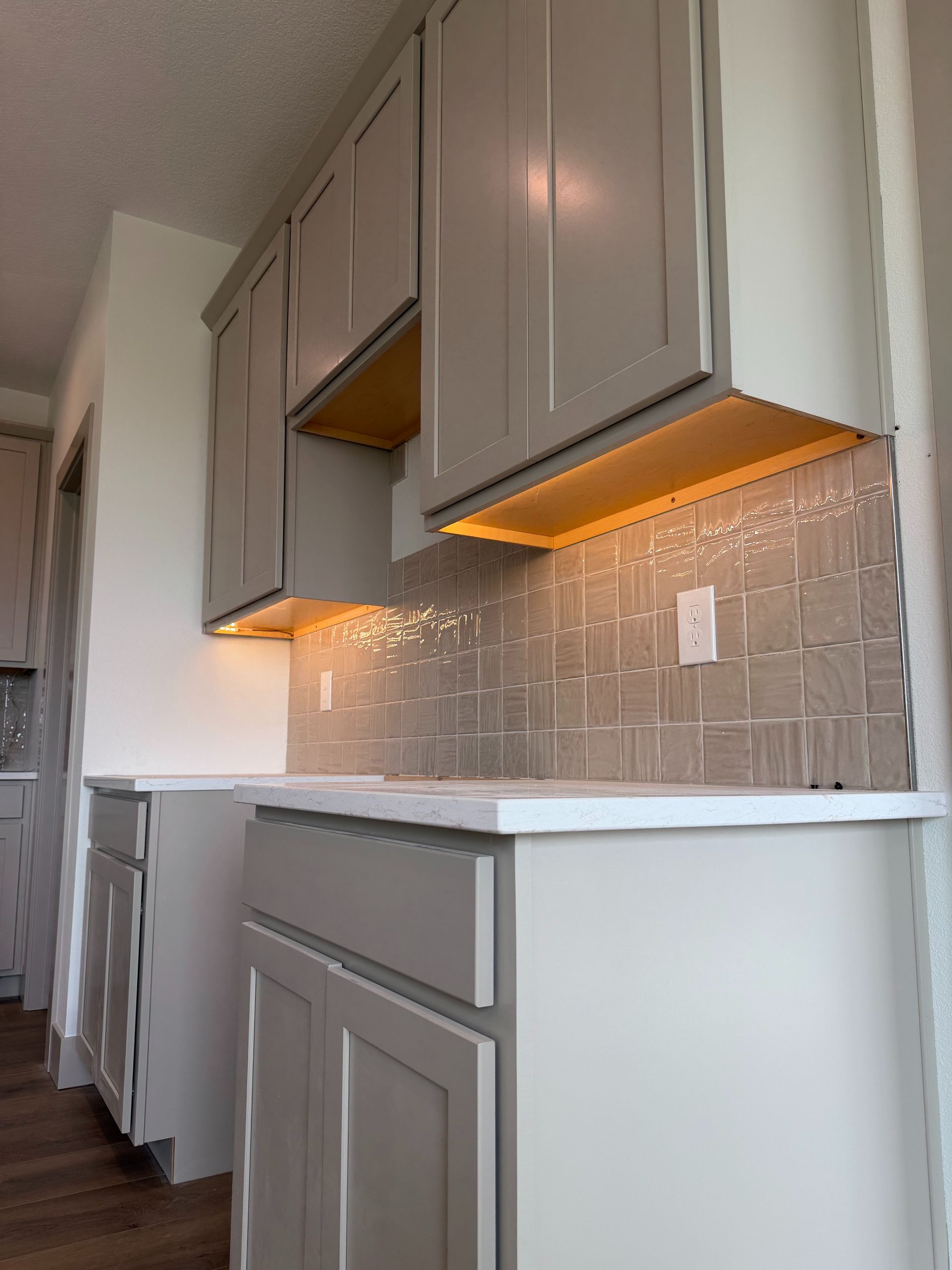 Modern kitchen hallway with gray cabinets, white countertops, and warm under-cabinet lighting