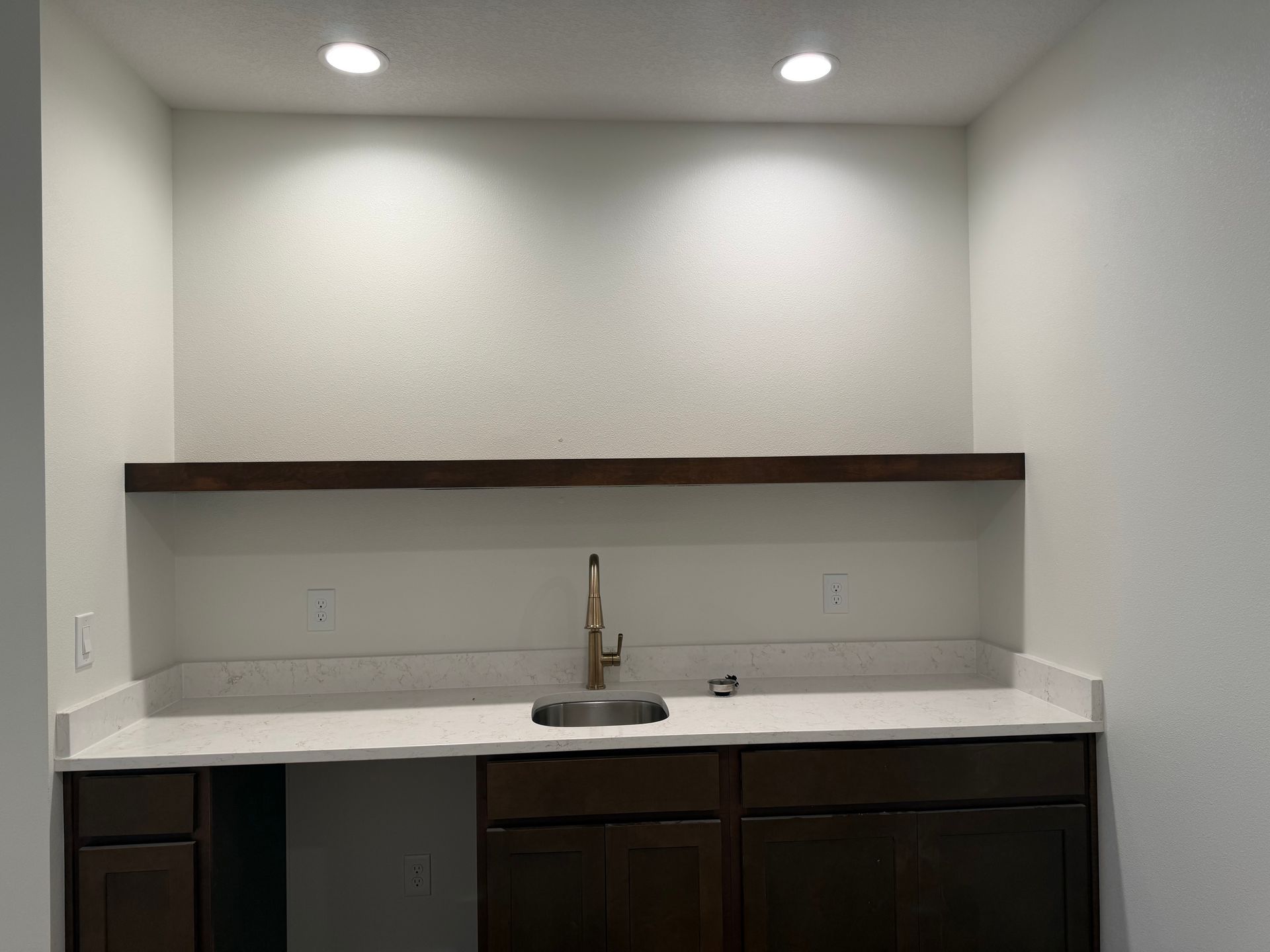 Empty built-in bar nook with white countertop, dark cabinets, sink, and overhead lights