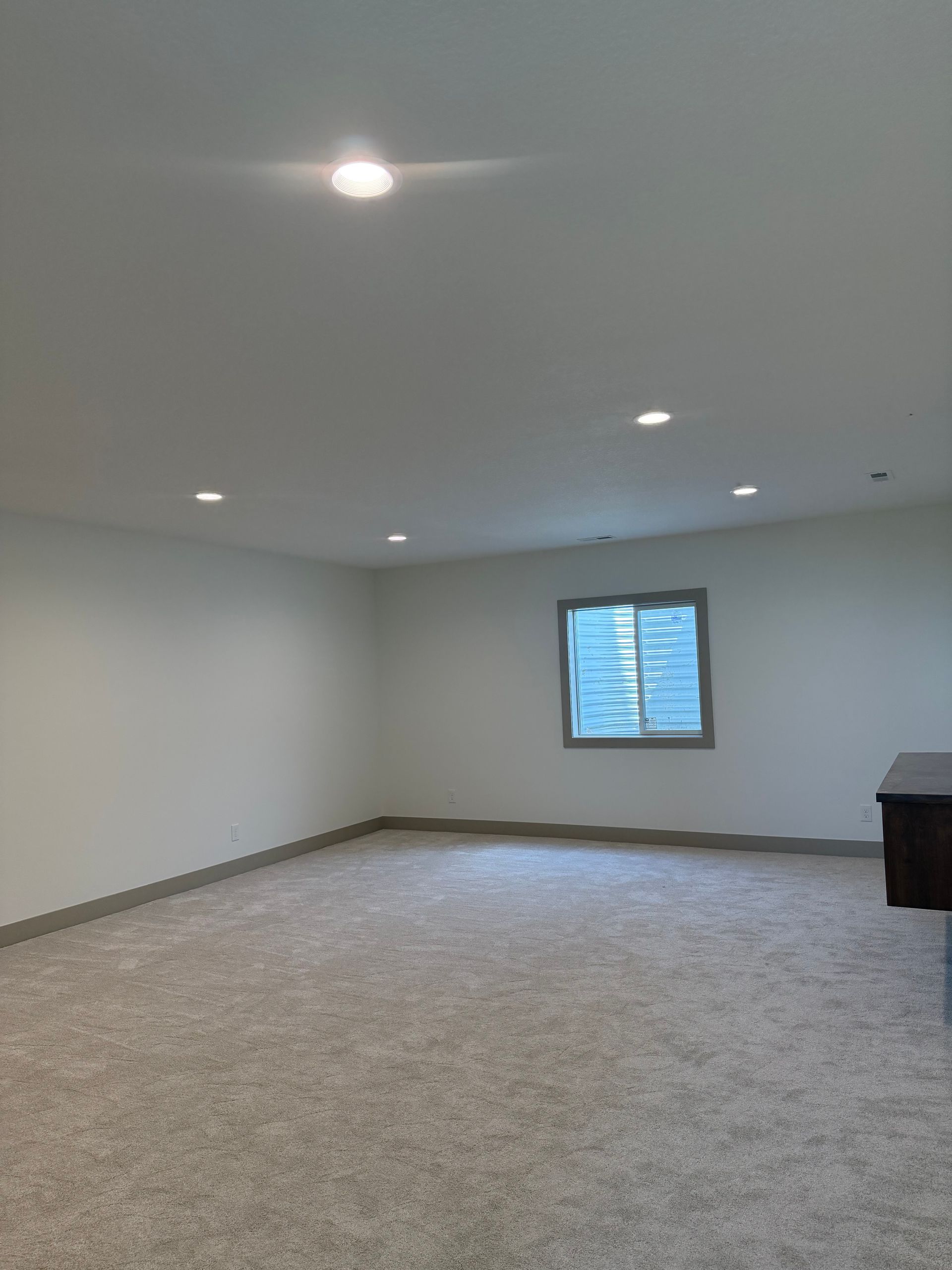 Empty carpeted room with gray walls, recessed lights, and a small window