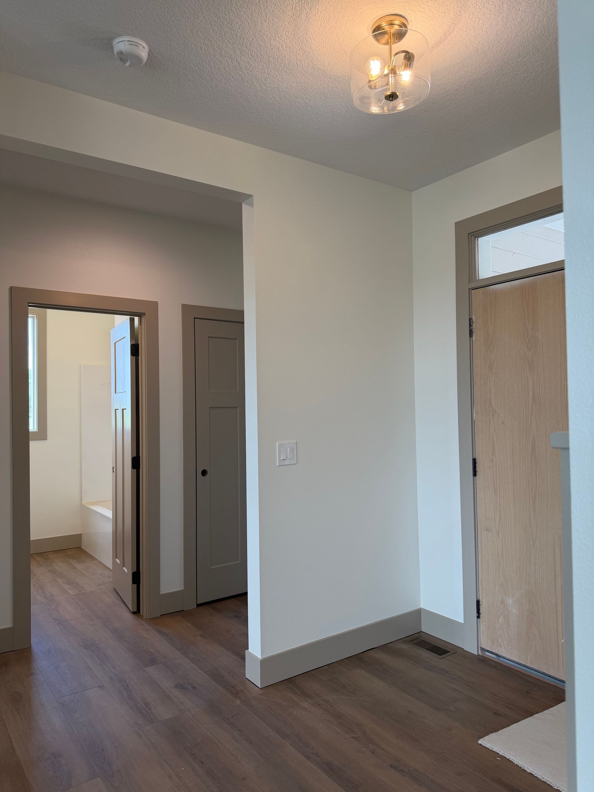 Empty hallway with white walls, wood floors, and two closed doors under a ceiling light.