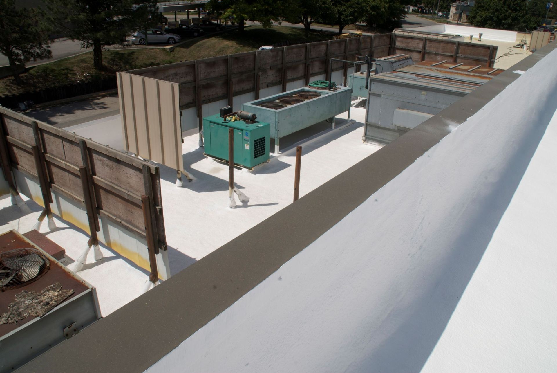 A rooftop scene with HVAC equipment, a green generator, and a wooden privacy wall on a white surface.