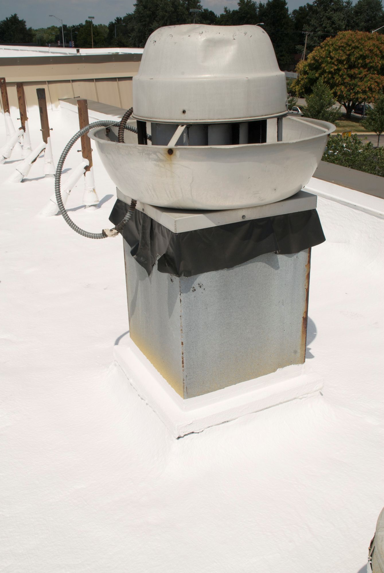 A white roof exhaust fan mounted on a square metal curb on a white flat commercial roof.