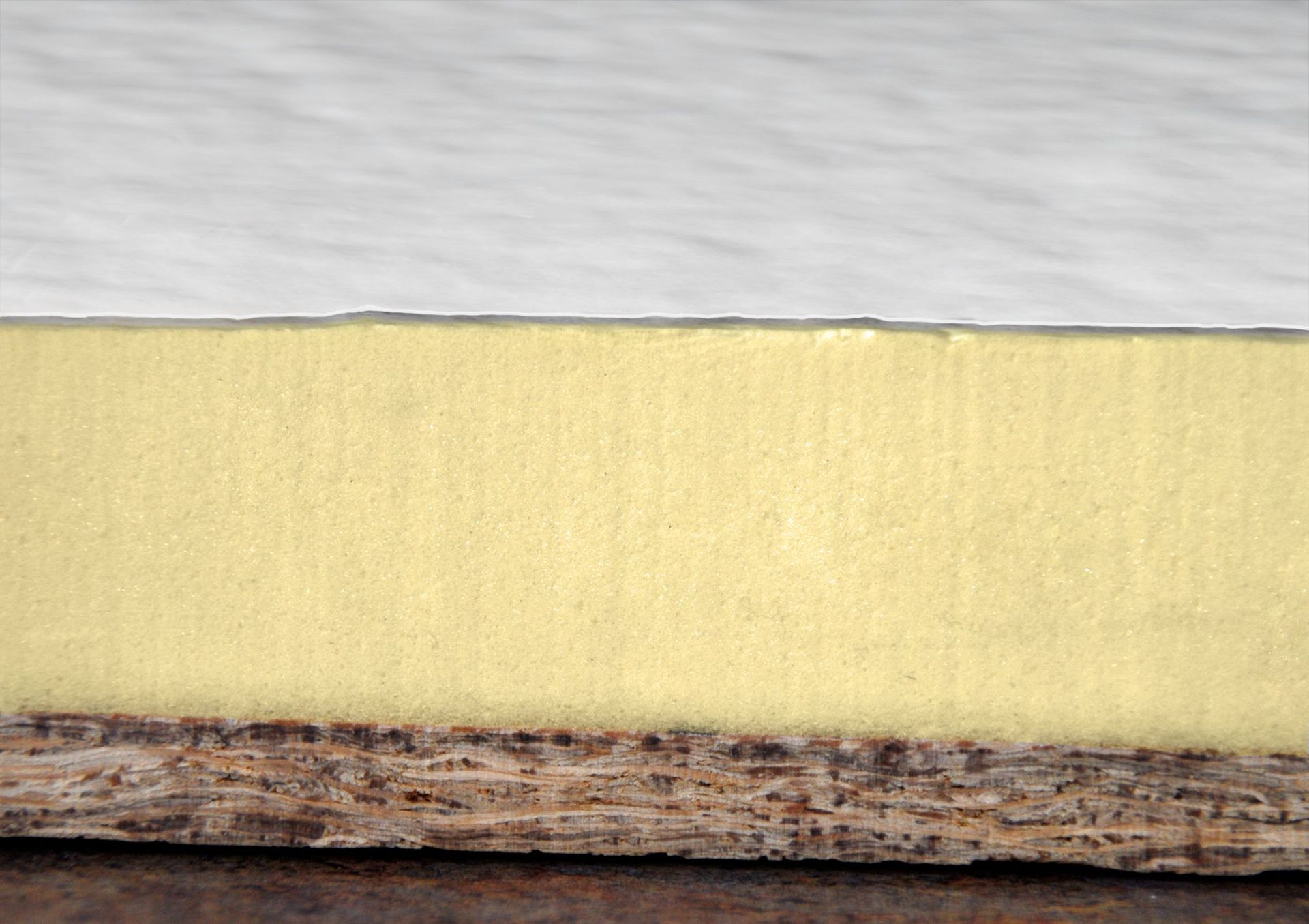 A side-view cross-section showing a thick layer of yellow foam insulation adhered to a dark, textured particle board base.
