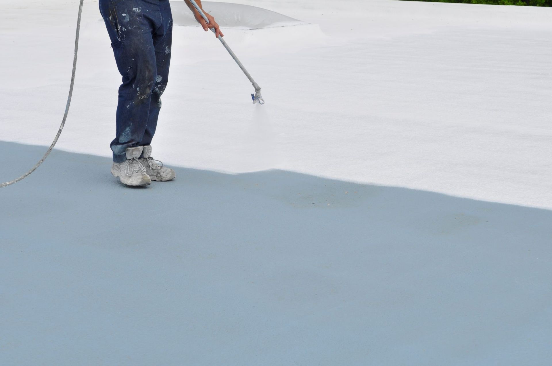 A worker sprays a white protective coating onto a grey roof surface.