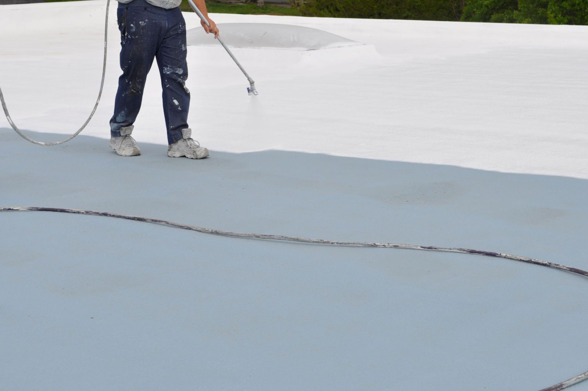 A worker sprays a white protective coating onto a flat gray roof.