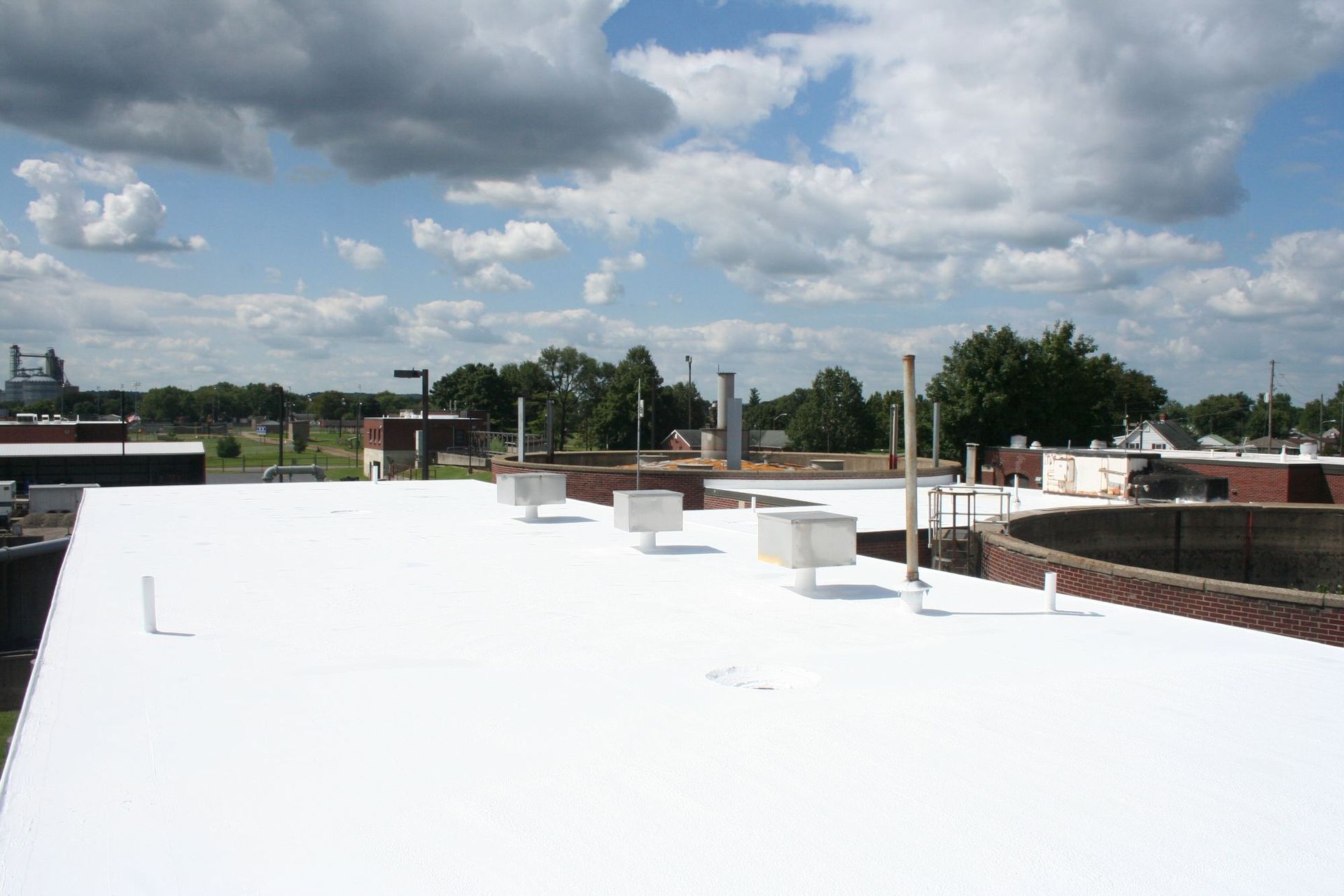 A bright white roof with several small vents and pipes under a partly cloudy blue sky.
