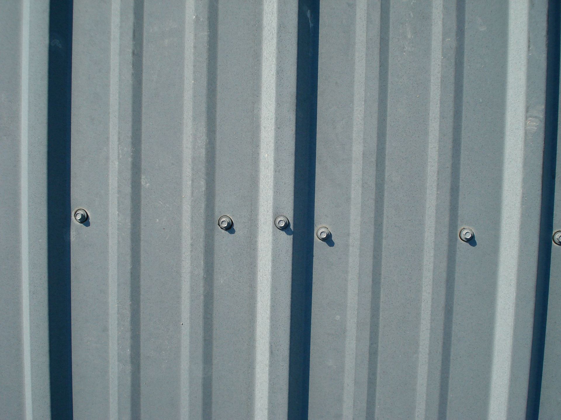 A close-up view of grey, vertically corrugated metal siding panels fastened with small, evenly spaced silver screws.
