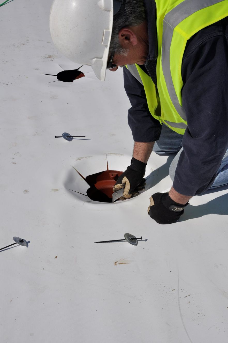 A person in a safety vest and hard hat installing a roof drain on a white membrane roof.