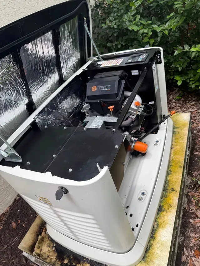 Open utility generator with black top cover and orange engine on a wet concrete surface