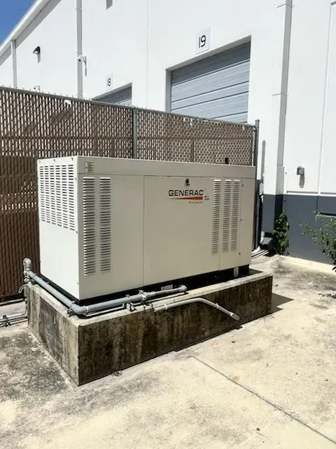 White outdoor generator unit on a concrete pad beside a building wall.
