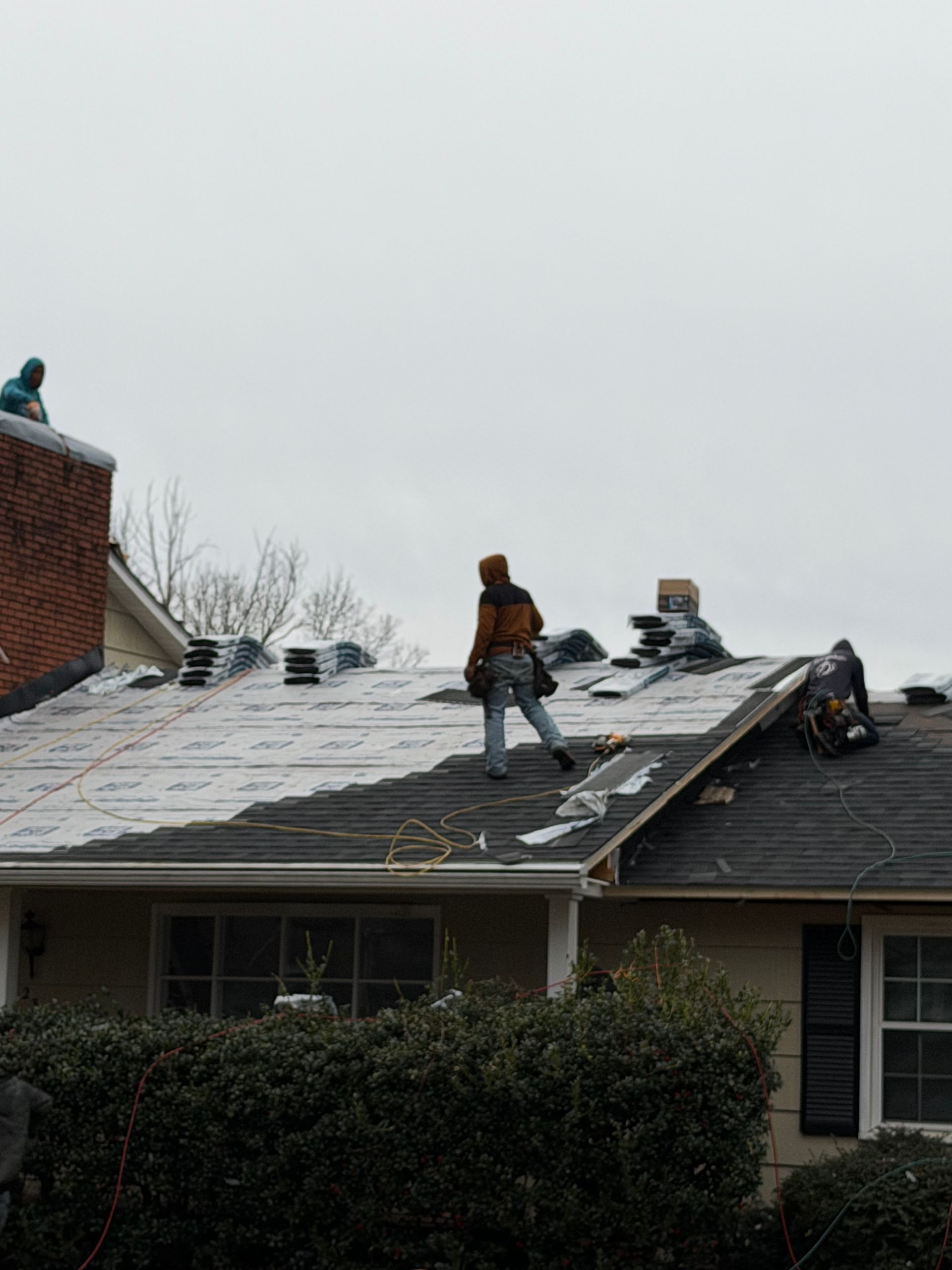 Construction workers replace asphalt shingles on a residential roof.