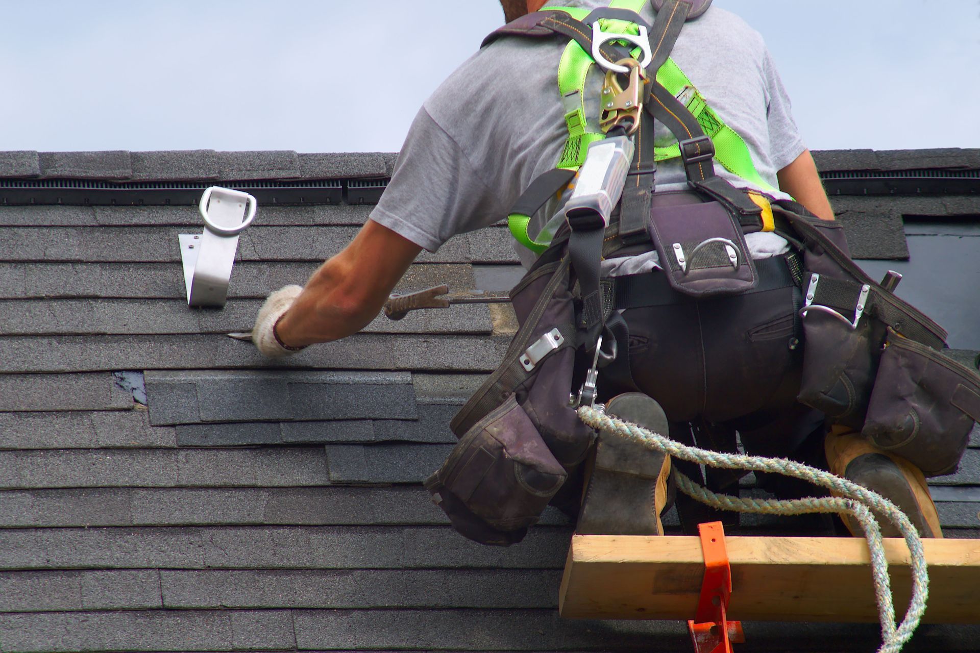 Roofer wearing safety harness on a roof, working on a fixture.