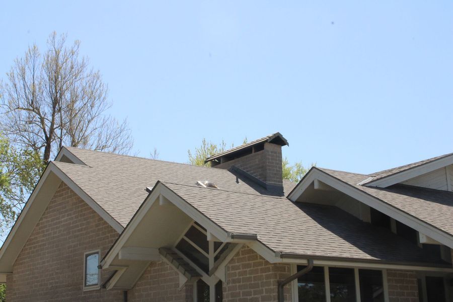 Brick house with gray shingled roof, chimney, and blue sky.