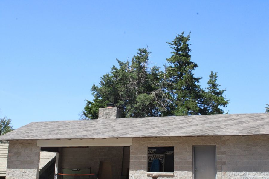 A light brown building with a gray roof and chimney, blue sky, and green trees.