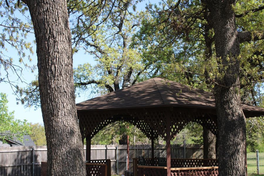 Gazebo under trees with brown roof and lattice details.
