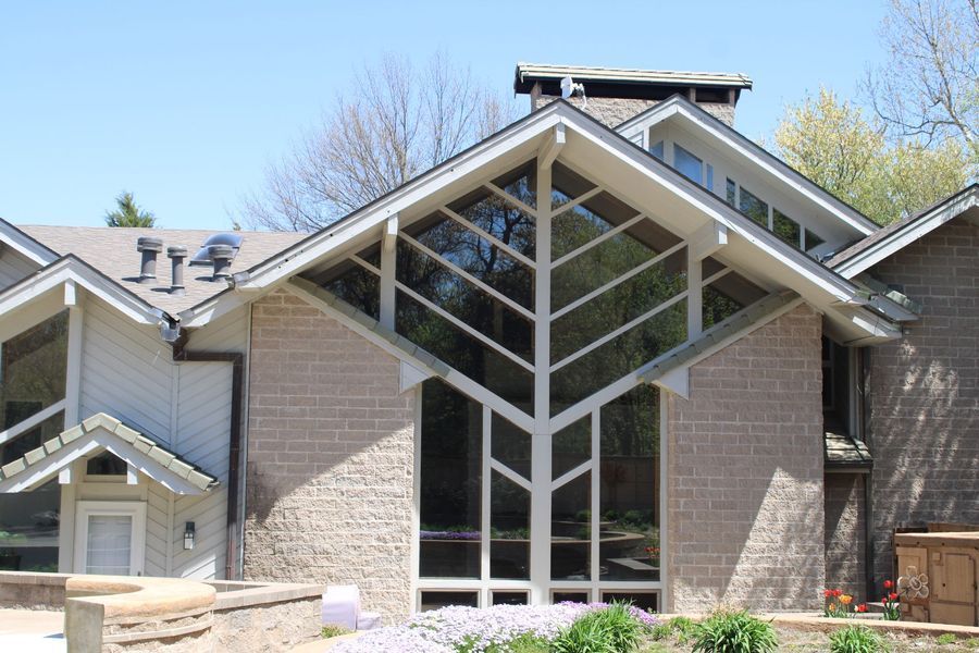 Beige brick house with large tree-shaped window, surrounded by trees and a blue sky.