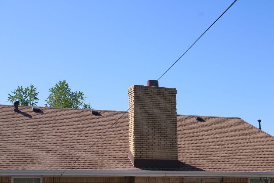 Brown roof with brick chimney, power line above. Blue sky.