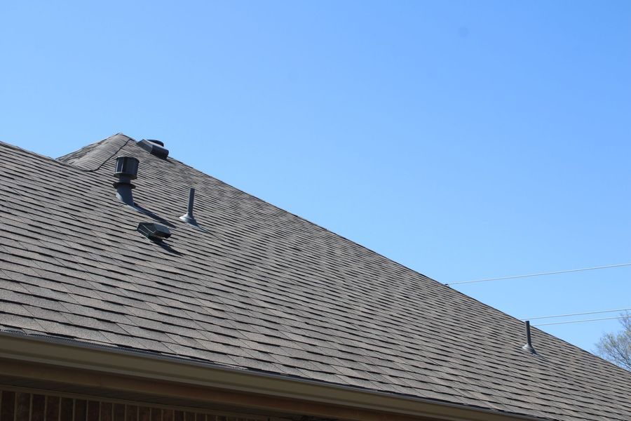 Dark gray shingled roof with multiple vents against a clear blue sky.