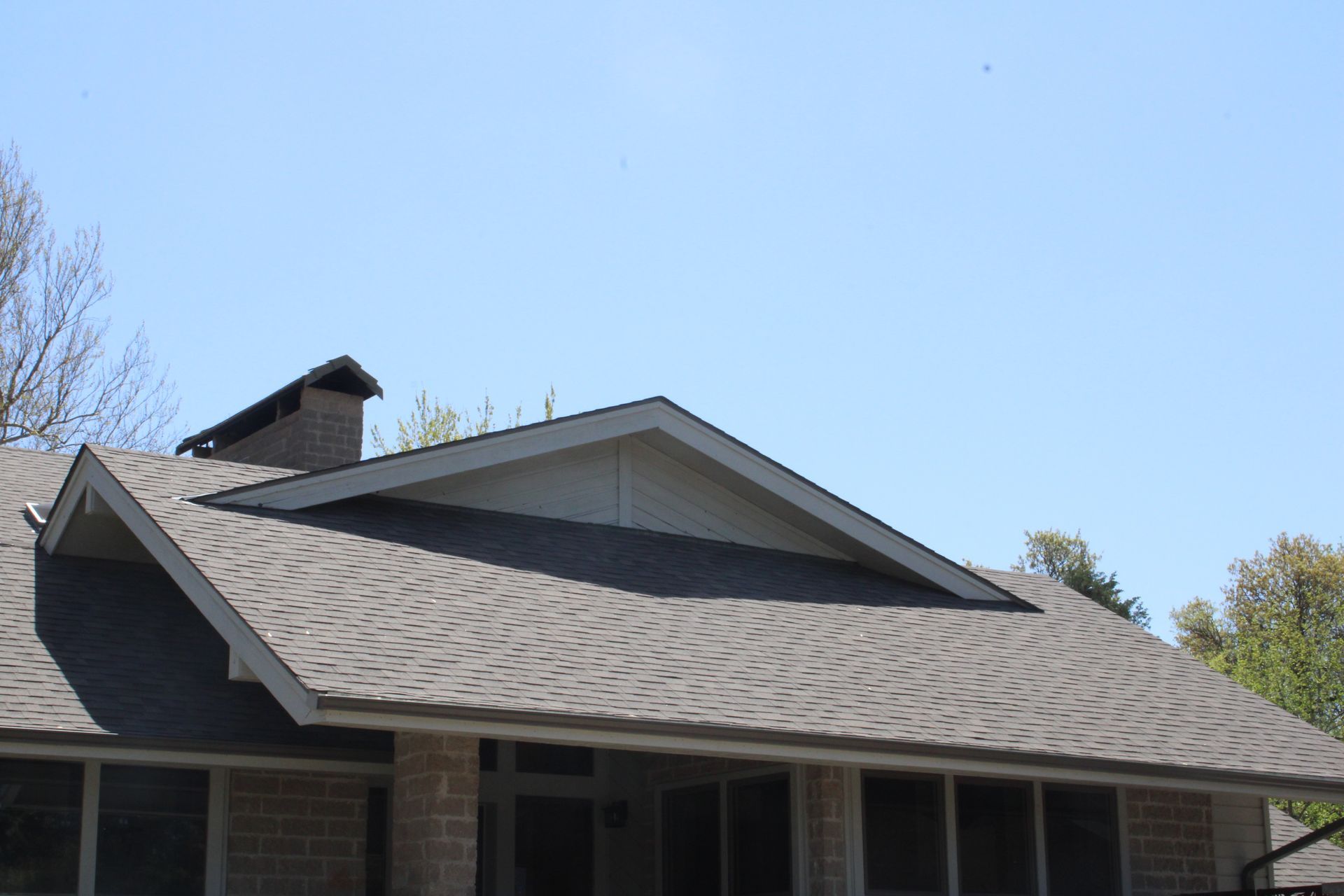 A house with a dark shingle roof, chimney, and blue sky in the background.