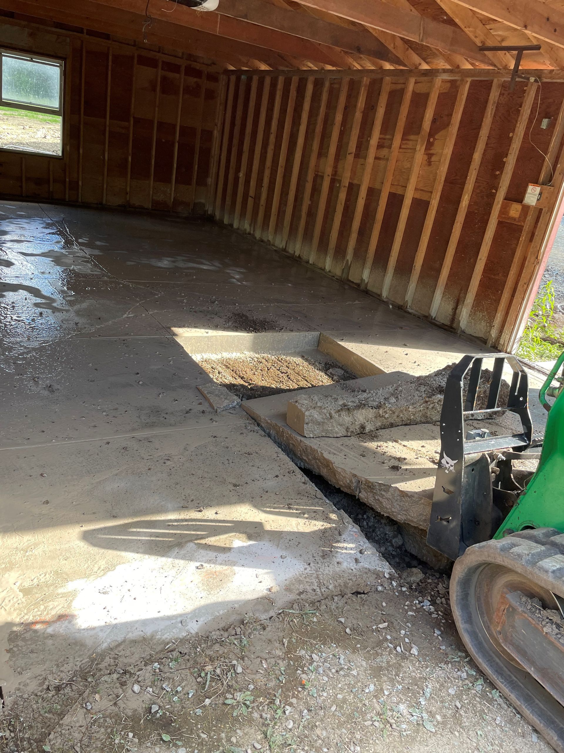 A green excavator is sitting in a garage under construction