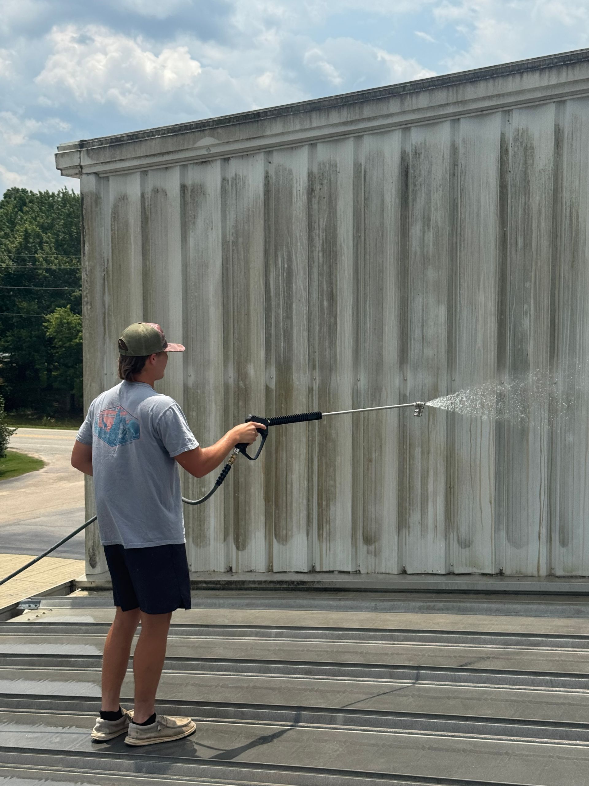 A man is cleaning a building with a high pressure washer.