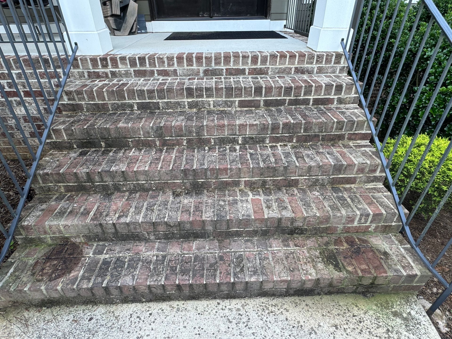 A set of brick stairs leading up to a house with a wrought iron railing.