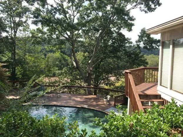 Backyard pool and deck beside a house, surrounded by trees and greenery
