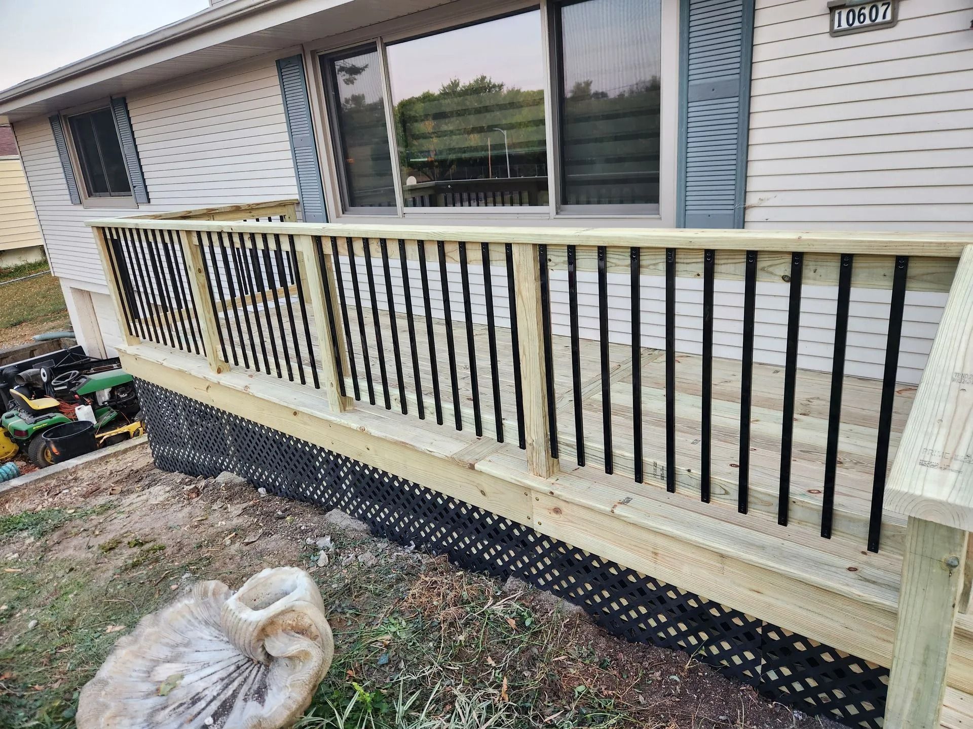 Wooden deck with black railing in front of a house. Black lattice siding below deck.