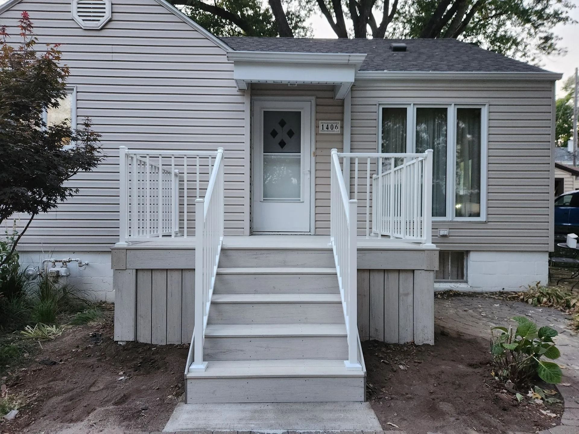 A small house with a front porch and steps. White railing and neutral-colored siding.