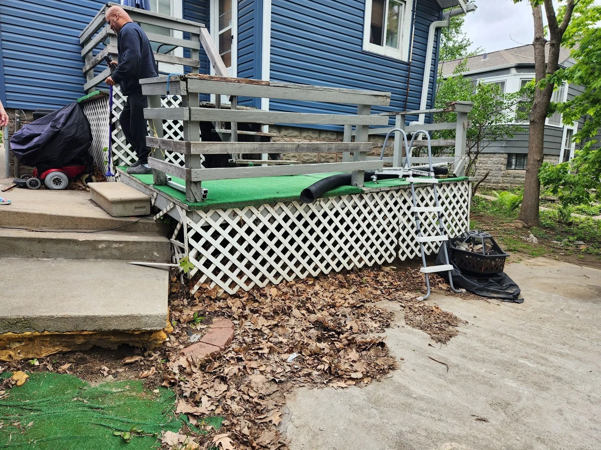 Deck of a blue house with a person, steps, and debris on the ground.