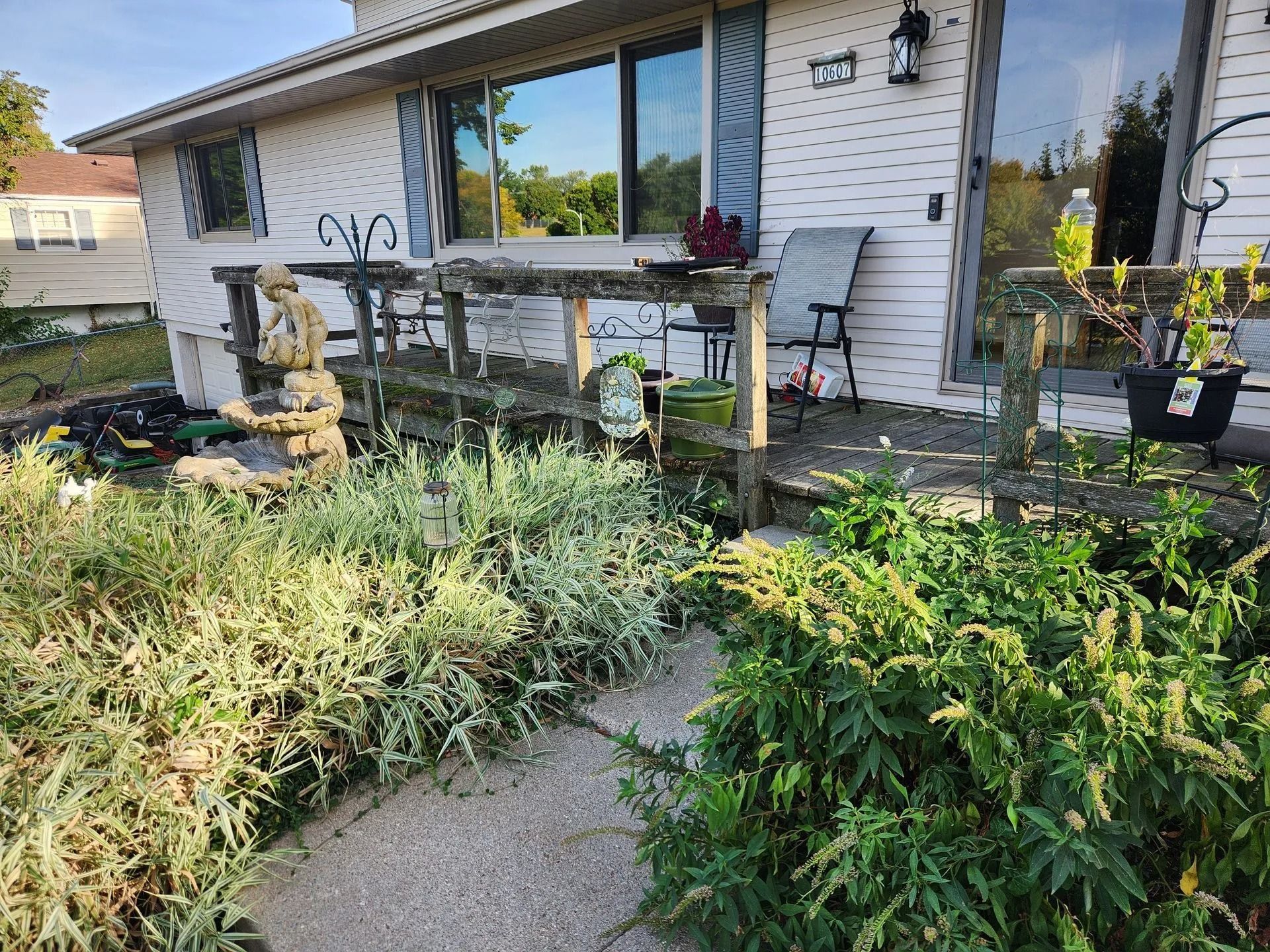 Exterior of a white house with overgrown garden and a small porch with seating.