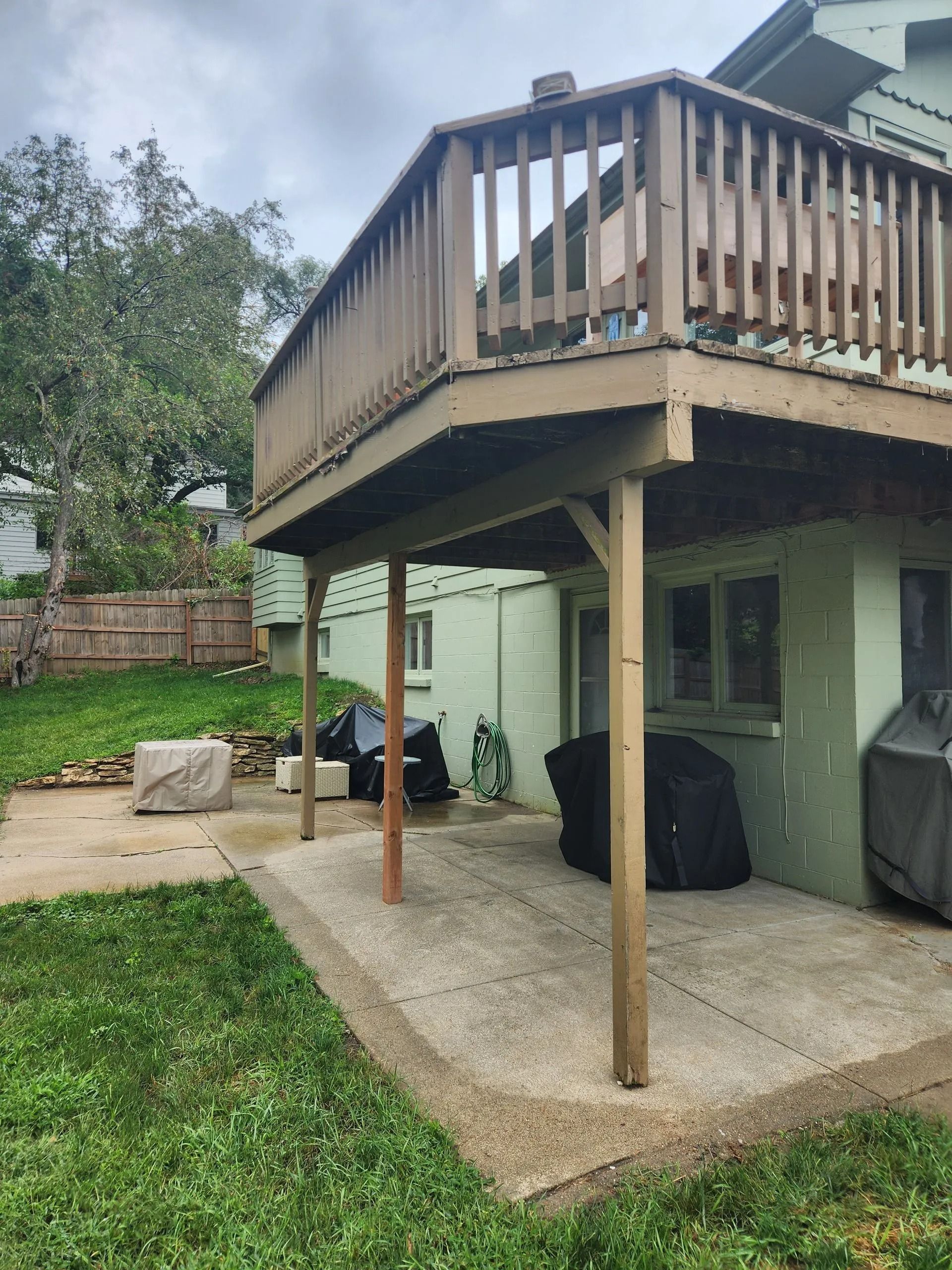 A two-story house with a wooden deck over a concrete patio.