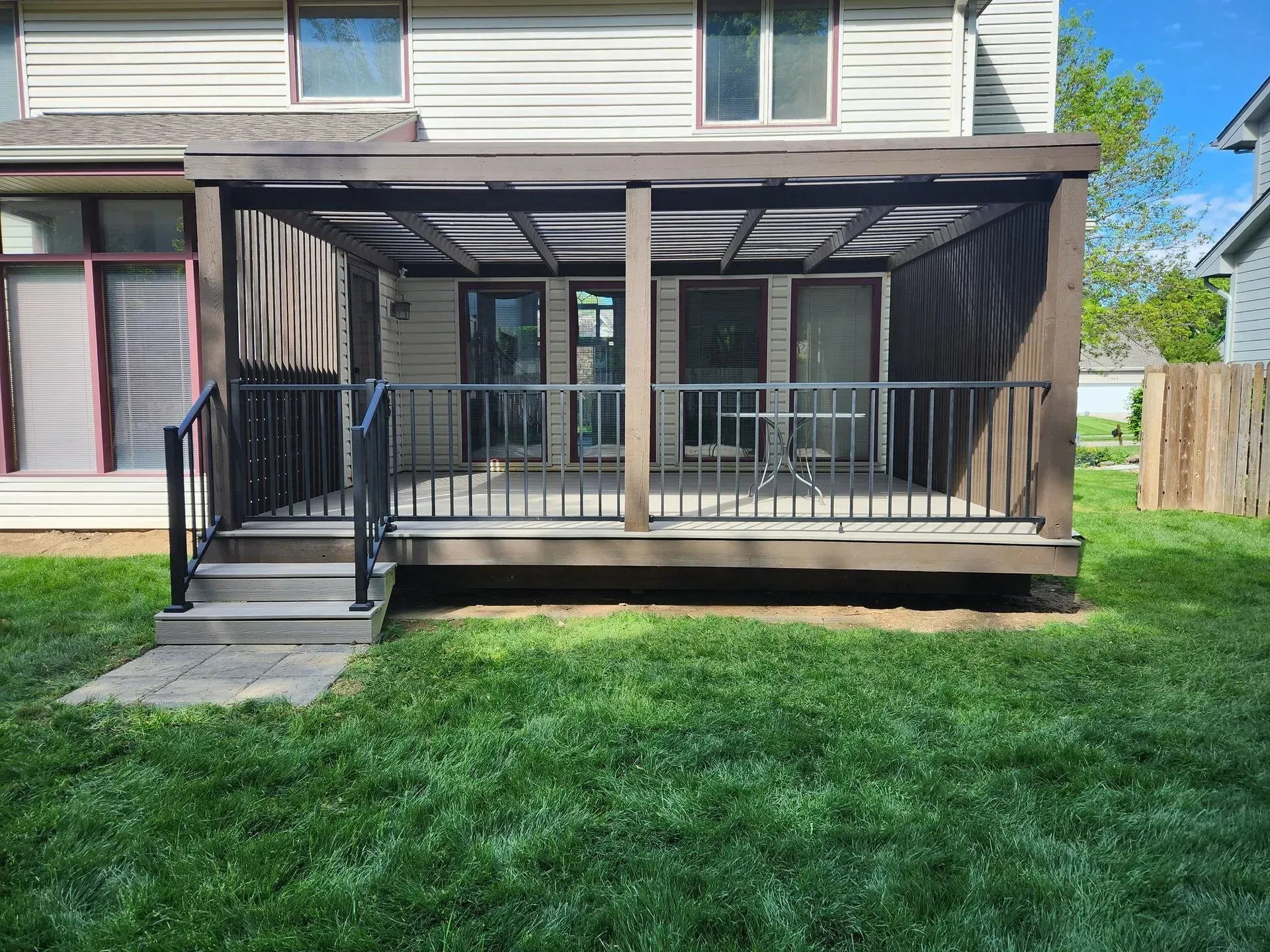 Dark brown deck with railing, pergola, and outdoor furniture in a backyard with green grass.