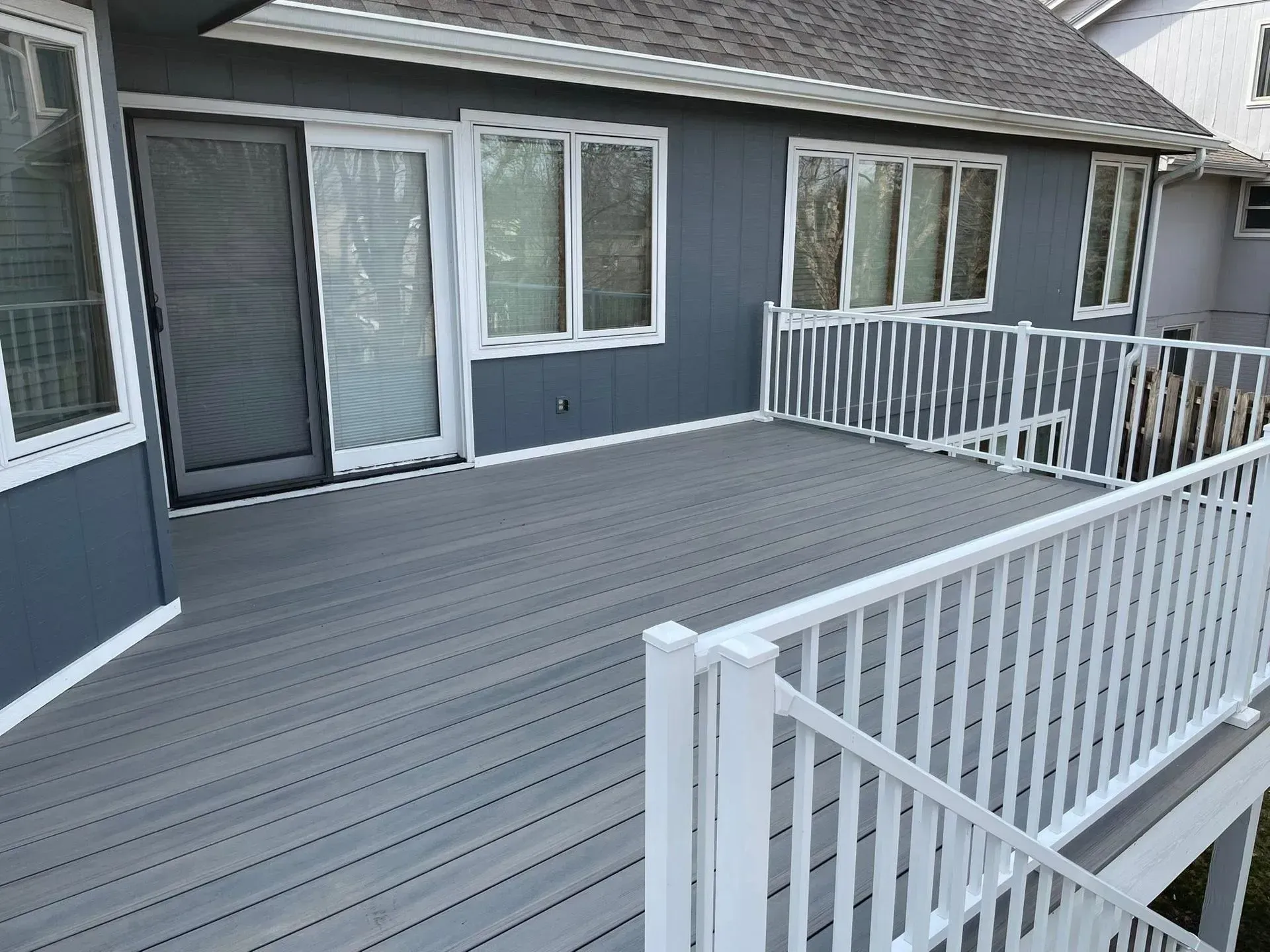 Gray composite deck with white railing next to a blue house with white trim.