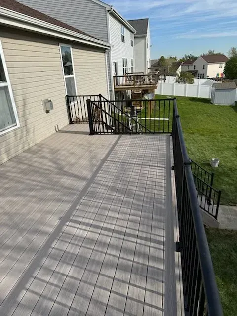 A gray composite deck with black railings and a ramp. Backyard with green grass and houses in the background.