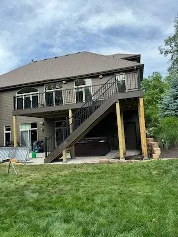Backyard view of a house with a multi-level deck, dark railings, and a hot tub underneath.