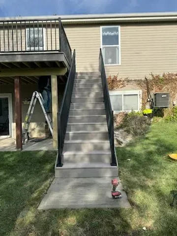 Outdoor stairs leading from a deck to a grassy yard, with black railing.