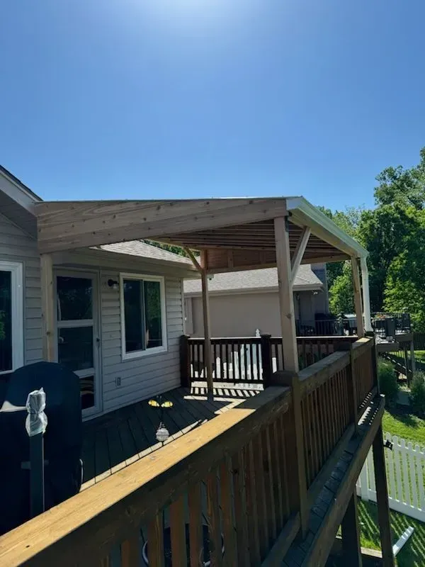 Wooden deck with pergola attached to a house, blue sky overhead.