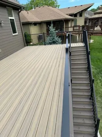 Composite deck with stairs and black railing next to a house with a brown roof.