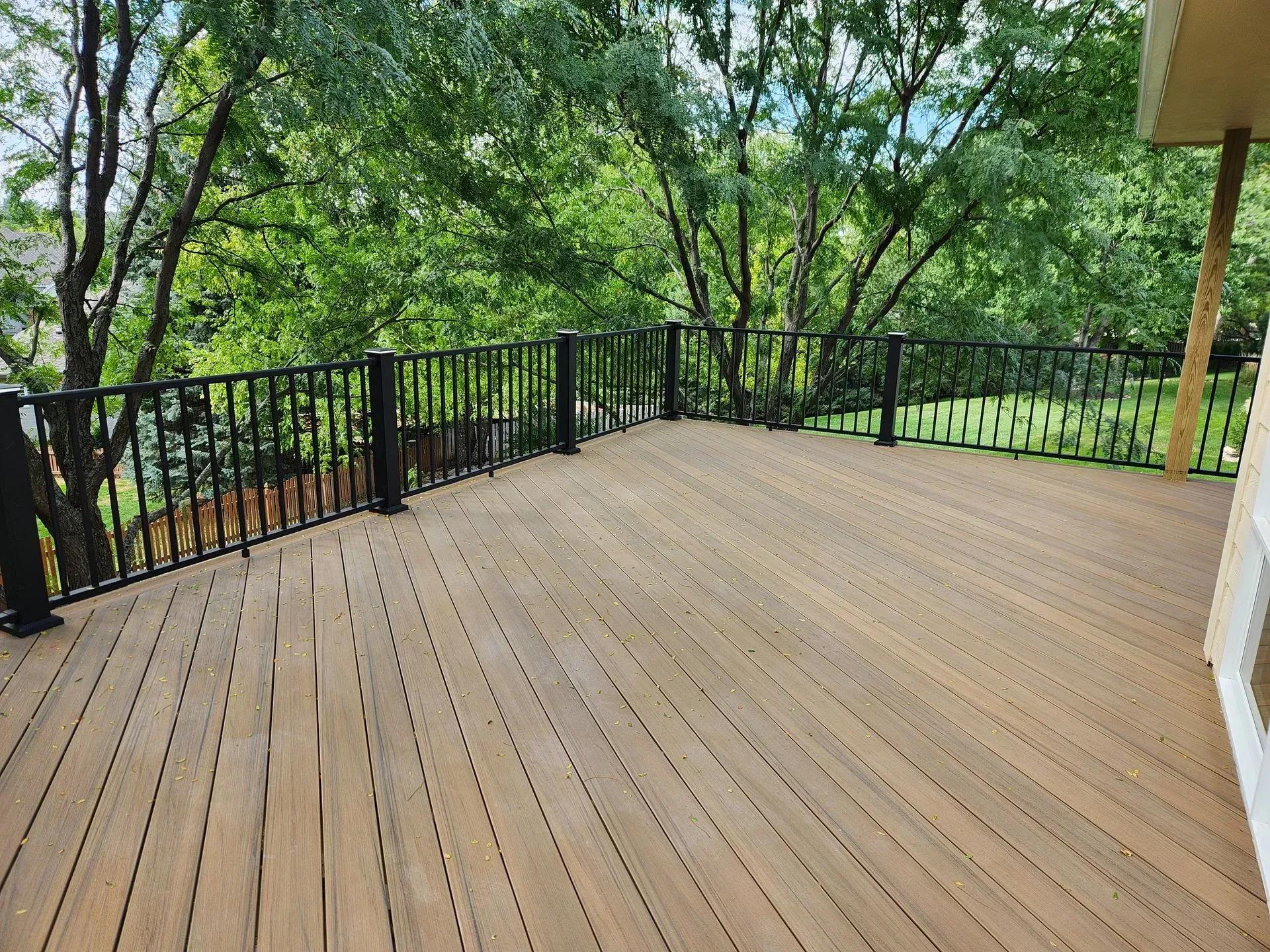 Wooden deck with black railings overlooking a green, tree-filled view.