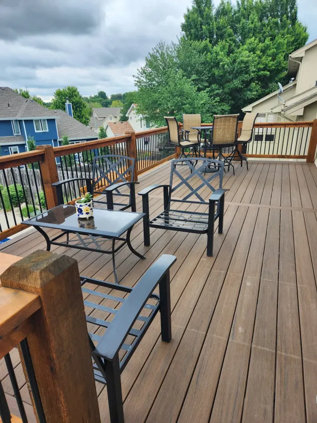 A wooden deck with black metal furniture, overlooking a neighborhood with cloudy sky.