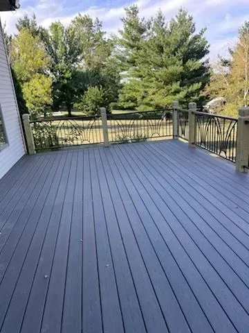 Gray wooden deck with black railings overlooking a treed yard on a sunny day.