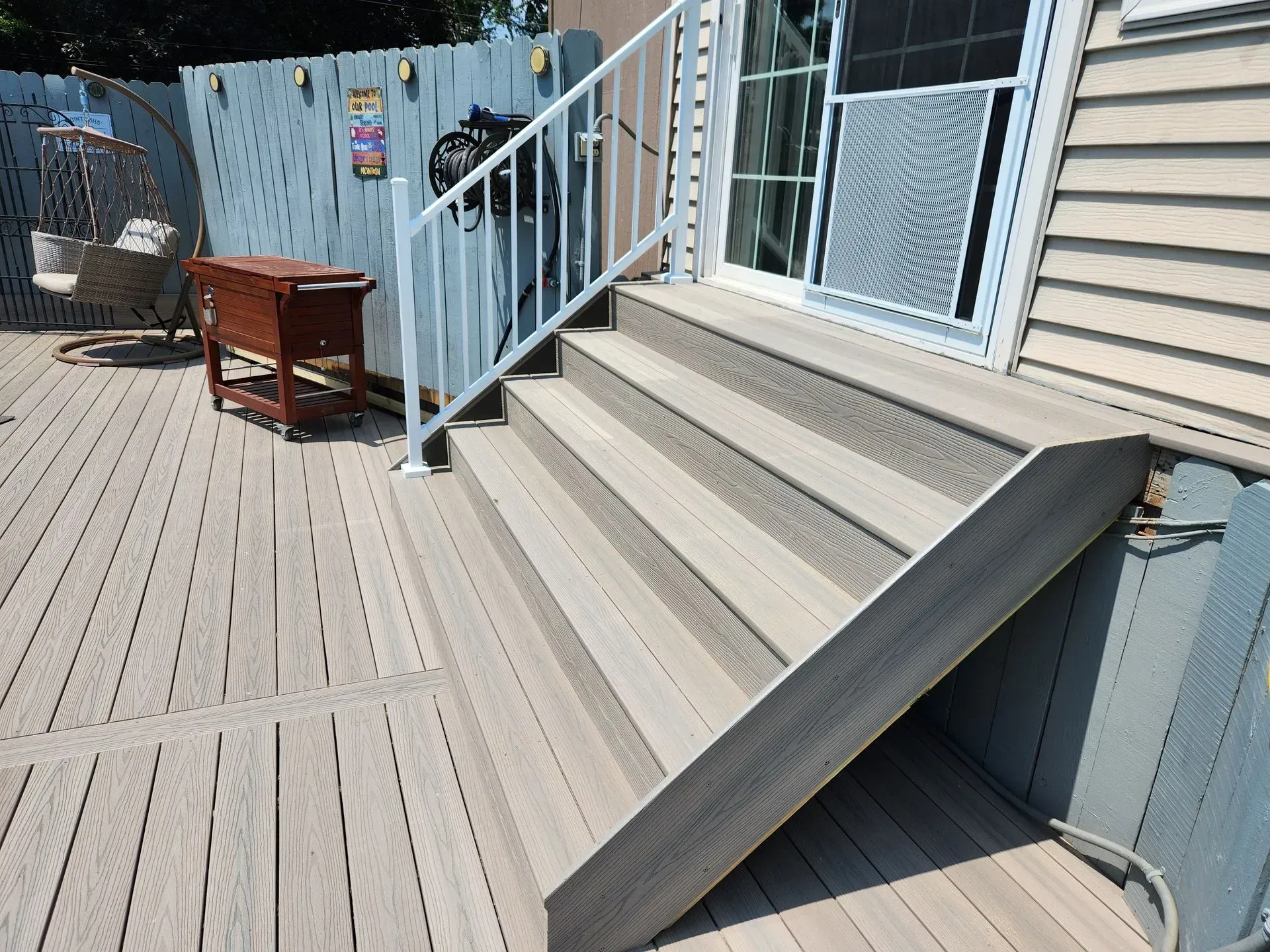 Deck with composite steps leading to a sliding glass door. White railing on the stairs.