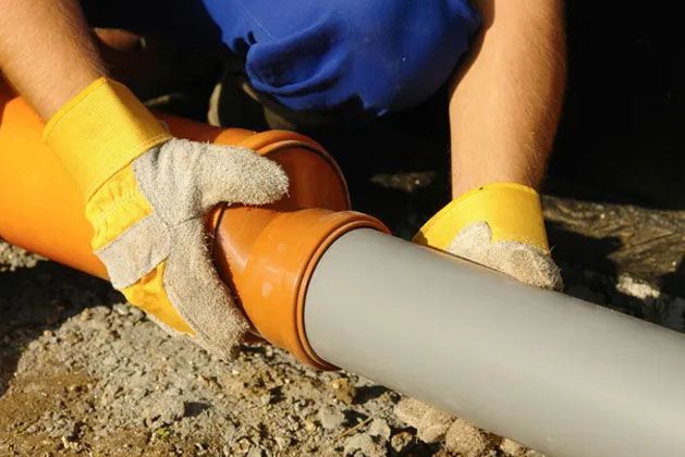 Hands in yellow gloves fitting an orange pipe coupling onto a gray pipe outdoors.