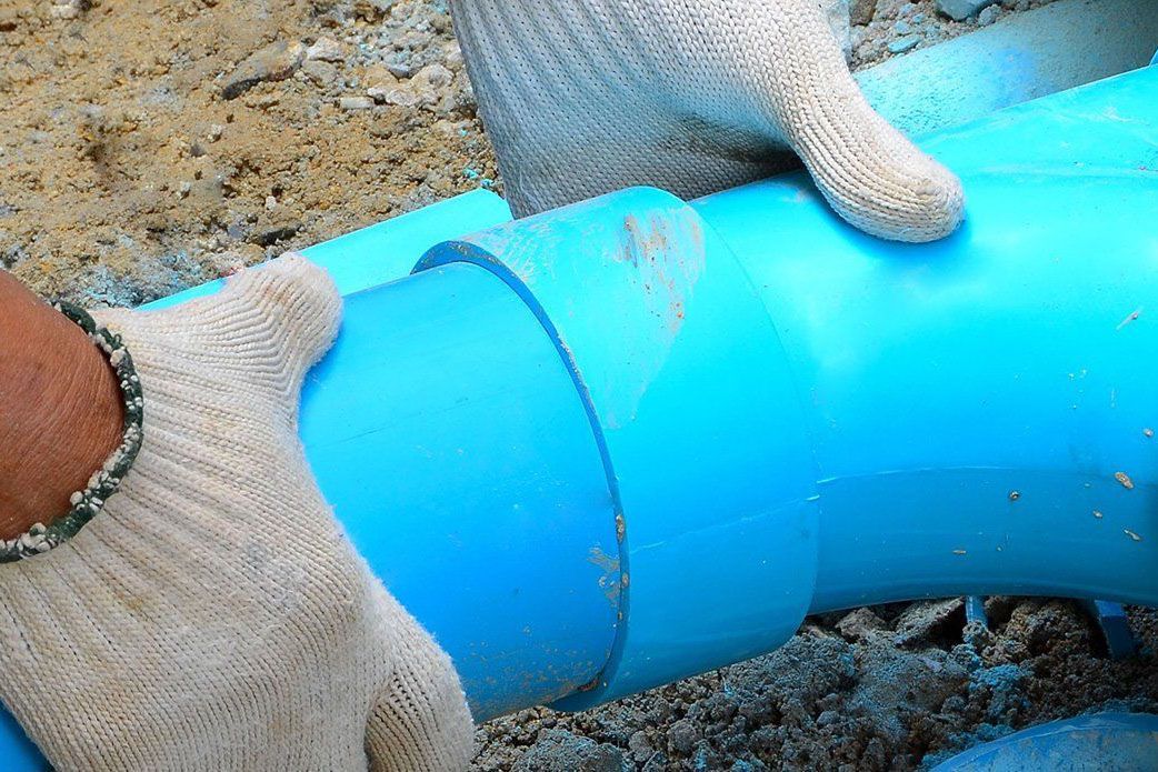 Gloved hands installing a bright blue pipe fitting in a trench
