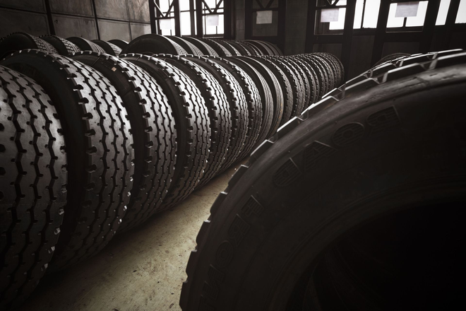 Rows of stacked tires in a dim warehouse, with a large tire in the foreground.