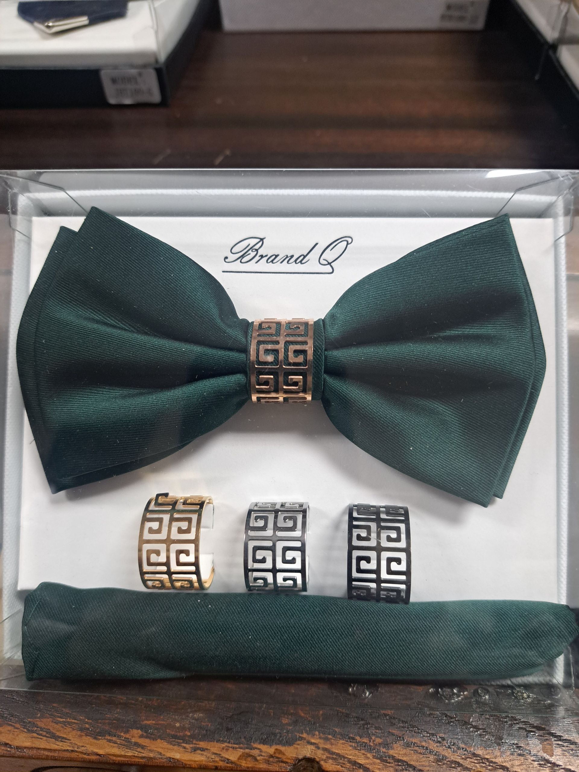 a green bow tie , pocket square , and rings are in a box .