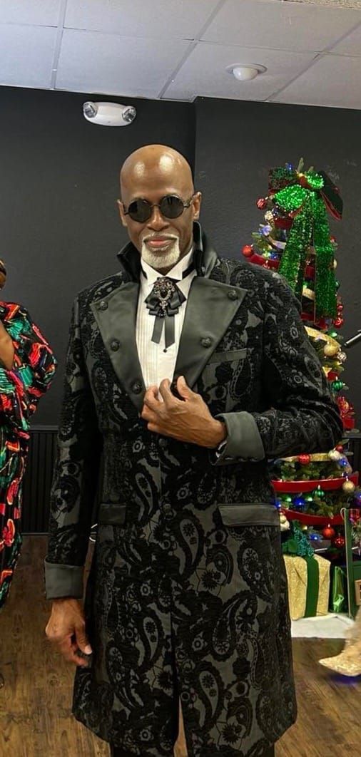 A man in a tuxedo and sunglasses is standing before a Christmas tree.