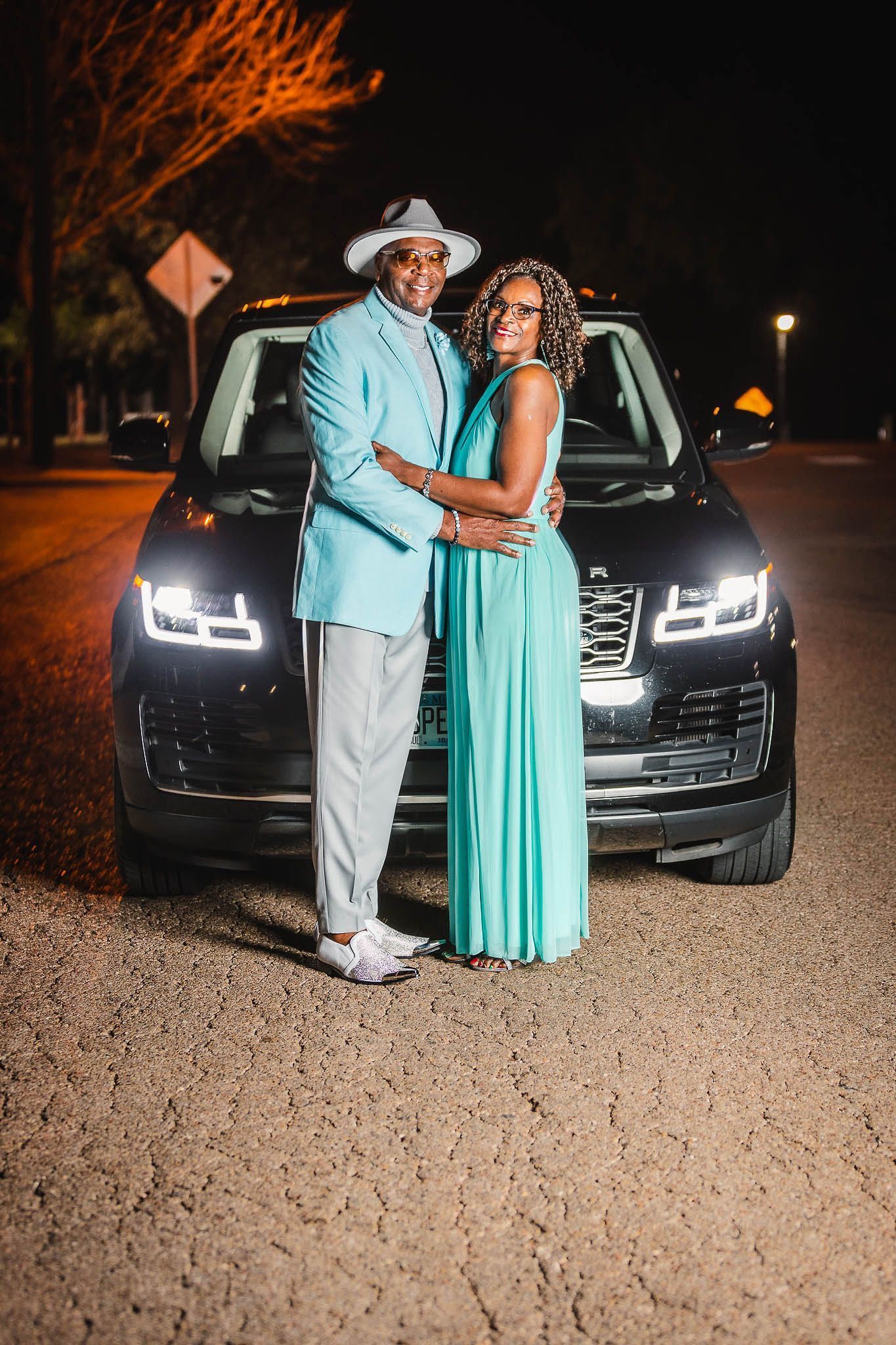 A man and a woman are posing for a picture in front of a car.